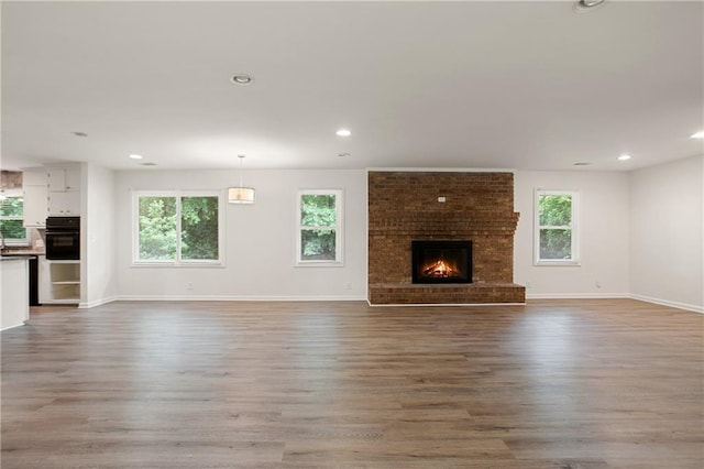 unfurnished living room with a fireplace, baseboards, wood finished floors, and a healthy amount of sunlight