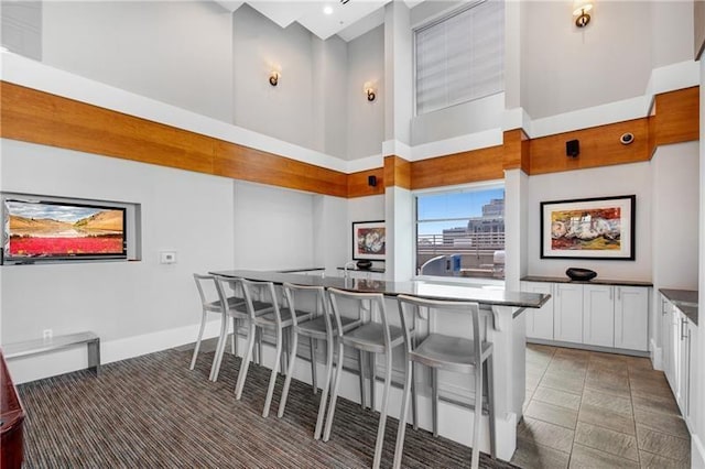 kitchen with white cabinets, dark countertops, baseboards, a high ceiling, and a breakfast bar