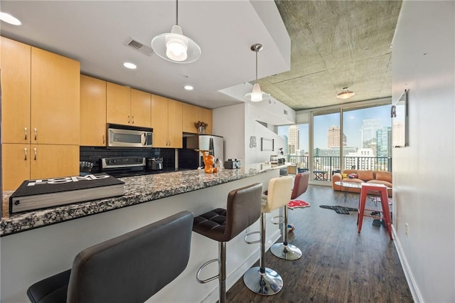 kitchen with stainless steel appliances, light brown cabinetry, visible vents, expansive windows, and dark wood-type flooring