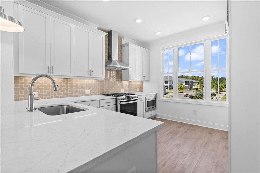 kitchen with stainless steel appliances, wall chimney exhaust hood, sink, white cabinetry, and light hardwood / wood-style flooring