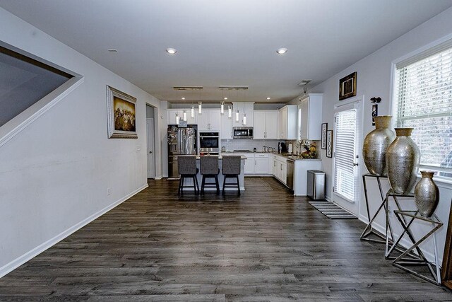 kitchen with stainless steel fridge, sink, a center island with sink, white cabinets, and hanging light fixtures