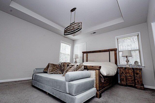 carpeted bedroom with a raised ceiling and an inviting chandelier