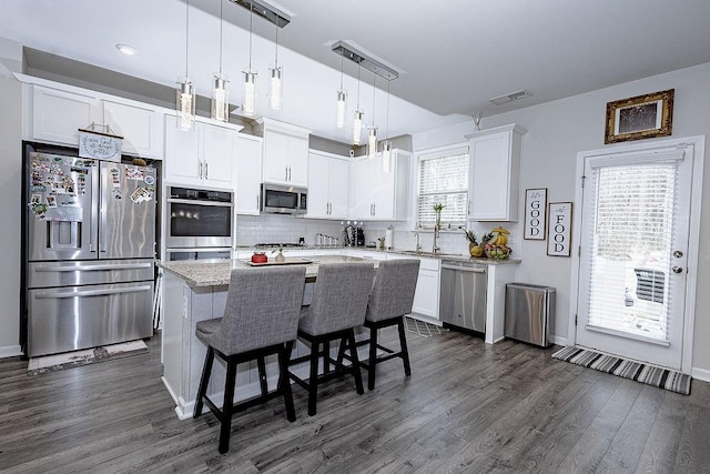 kitchen featuring stainless steel appliances, a kitchen island, visible vents, white cabinets, and decorative backsplash