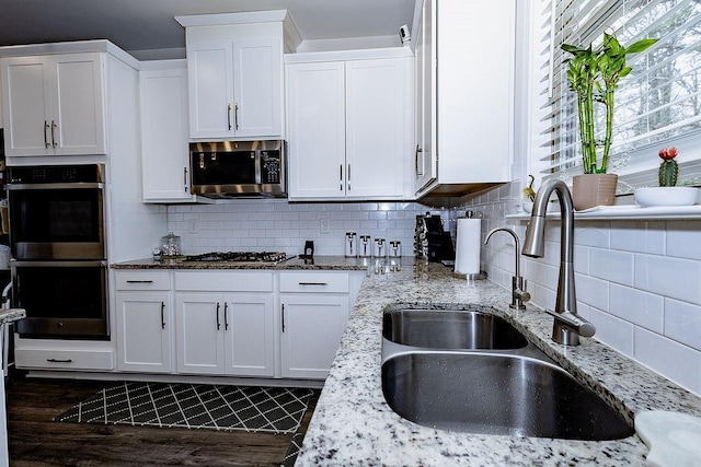 kitchen with stainless steel appliances, a sink, light stone countertops, and white cabinets