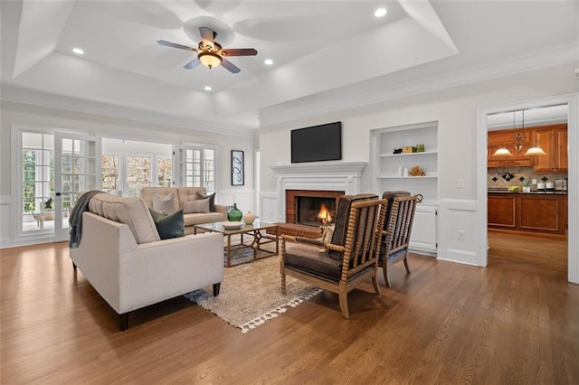 living room with a raised ceiling, hardwood / wood-style floors, a wealth of natural light, and built in shelves