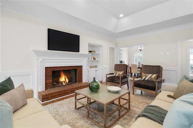 living room with crown molding, built in features, a notable chandelier, a fireplace, and light hardwood / wood-style floors