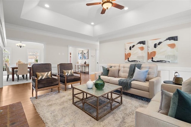 living room featuring a tray ceiling, light hardwood / wood-style flooring, ornamental molding, and ceiling fan with notable chandelier