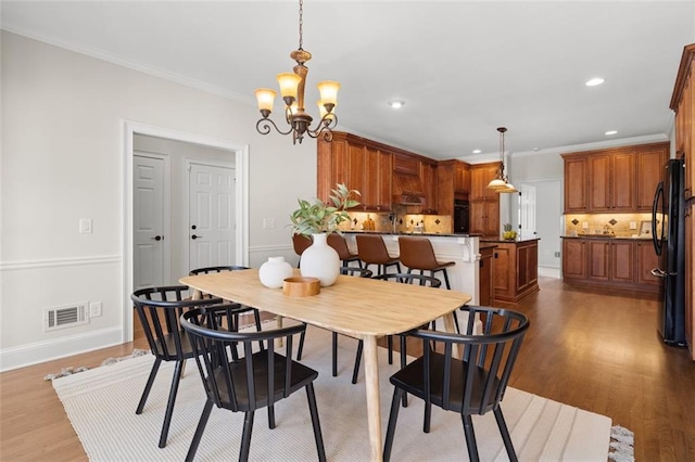 dining area featuring wood-type flooring, a notable chandelier, and crown molding