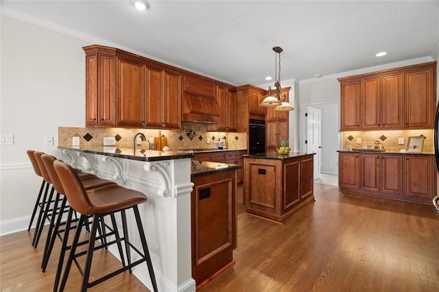 kitchen featuring pendant lighting, black oven, custom range hood, kitchen peninsula, and dark stone counters