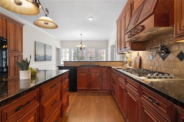 kitchen featuring sink, premium range hood, black dishwasher, stainless steel gas cooktop, and decorative light fixtures