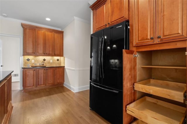 kitchen with black fridge, ornamental molding, decorative backsplash, and light hardwood / wood-style flooring