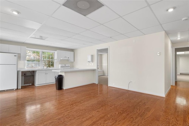 kitchen featuring a paneled ceiling, white cabinets, white appliances, kitchen peninsula, and light wood-type flooring