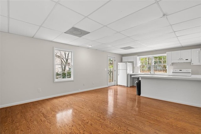 kitchen with white appliances, a paneled ceiling, light hardwood / wood-style floors, and white cabinets