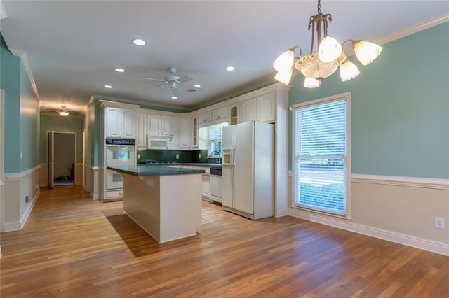 kitchen with white appliances, a kitchen island, dark countertops, white cabinetry, and crown molding