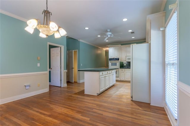 kitchen featuring white appliances, ornamental molding, a kitchen island, recessed lighting, and dark countertops