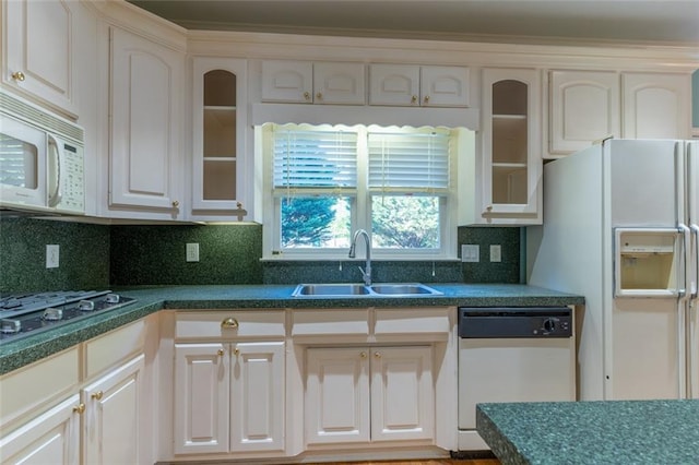 kitchen with white appliances, a sink, dark countertops, glass insert cabinets, and tasteful backsplash