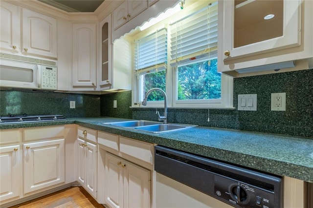 kitchen with white microwave, dishwashing machine, a sink, and dark countertops