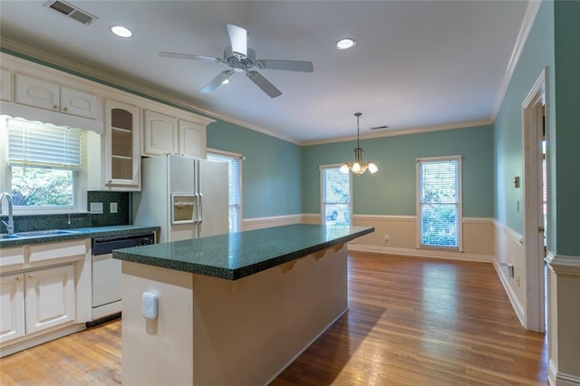 kitchen featuring a sink, white appliances, dark countertops, a kitchen island, and ornamental molding