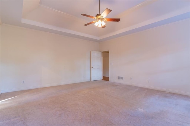 carpeted spare room featuring a raised ceiling, baseboards, a ceiling fan, and crown molding
