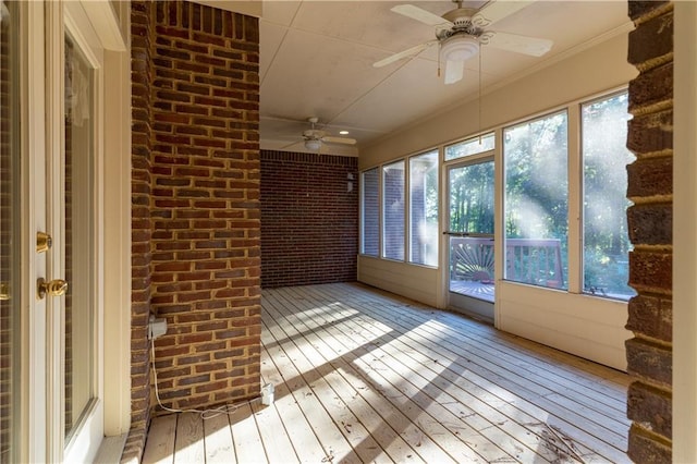 unfurnished sunroom featuring ceiling fan, brick wall, hardwood / wood-style flooring, ornamental molding, and a wooden deck