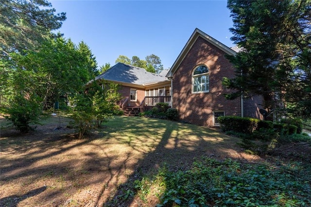 back of property featuring brick siding, a lawn, and a wooden deck
