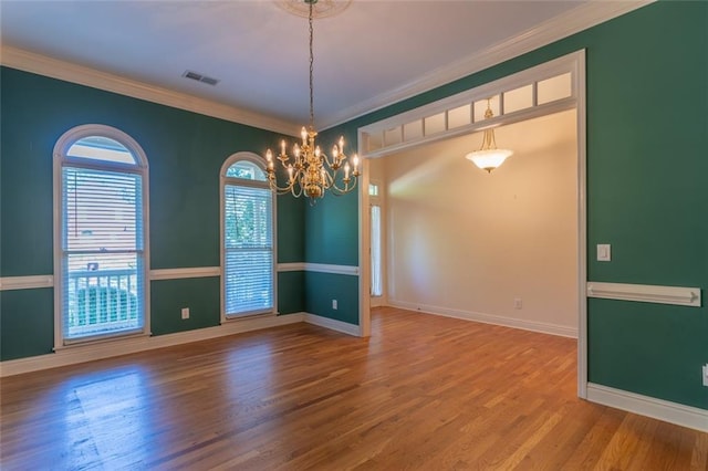 empty room with a chandelier, wood finished floors, baseboards, and crown molding