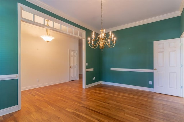 empty room featuring a chandelier, ornamental molding, wood finished floors, and baseboards