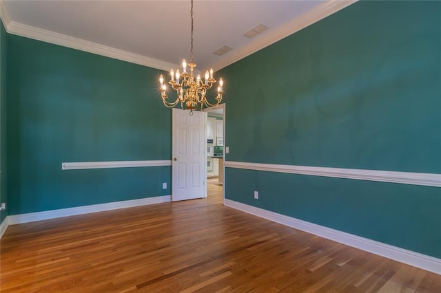 unfurnished room with a chandelier, wood finished floors, crown molding, and baseboards