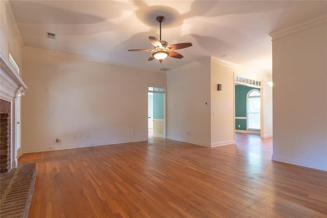 unfurnished living room with ceiling fan, wood finished floors, crown molding, arched walkways, and a brick fireplace