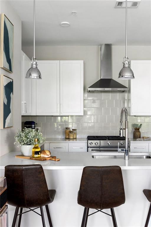 22 Airline St NE Unit 201, Atlanta, GA 30312 - kitchen featuring wall chimney range hood, a kitchen bar, white cabinets, and light countertops