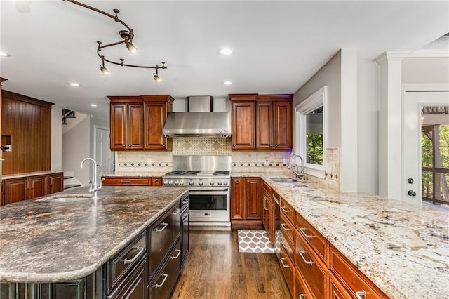 kitchen featuring high end range, wall chimney range hood, sink, and an island with sink