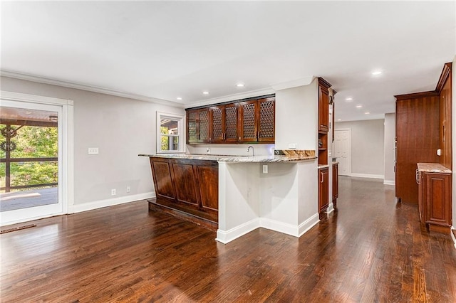 kitchen with dark wood-type flooring, a breakfast bar area, light stone counters, ornamental molding, and kitchen peninsula