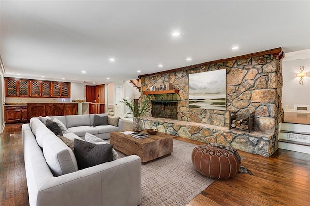 living room with dark wood-type flooring, bar, and a stone fireplace