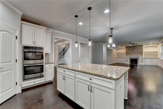 kitchen featuring a kitchen island, a ceiling fan, dark wood finished floors, and double oven