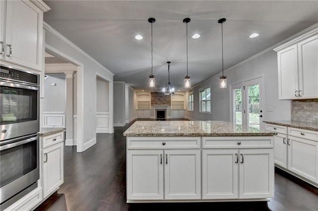 kitchen featuring hanging light fixtures, a fireplace, white cabinets, double oven, and ornamental molding