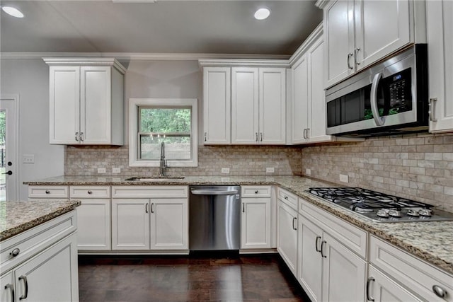 kitchen featuring white cabinets, appliances with stainless steel finishes, a sink, backsplash, and ornamental molding