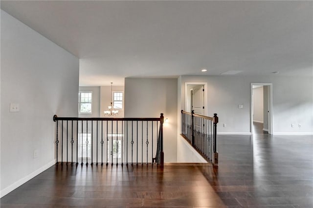 corridor featuring baseboards, an inviting chandelier, wood finished floors, and an upstairs landing