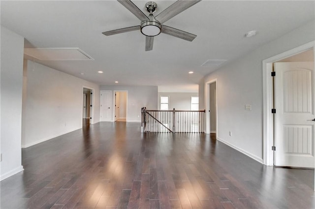 unfurnished living room with a ceiling fan, baseboards, dark wood finished floors, and attic access