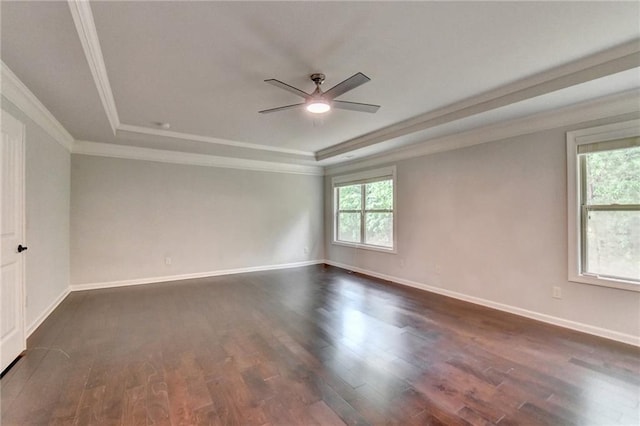 empty room featuring a ceiling fan, dark wood finished floors, a raised ceiling, baseboards, and ornamental molding