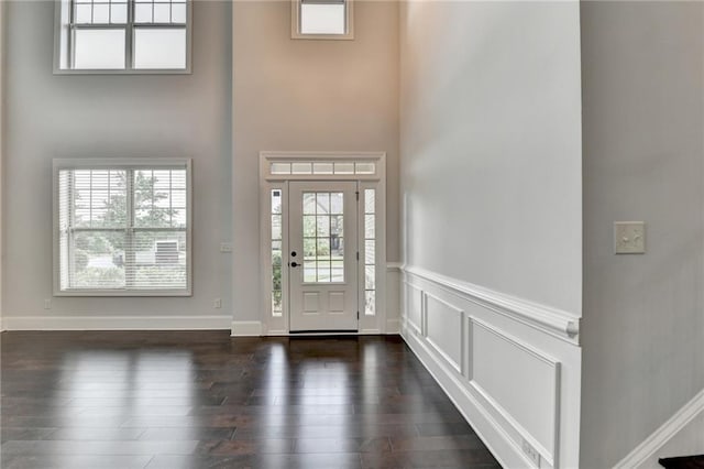 entrance foyer featuring a wainscoted wall, a wealth of natural light, dark wood-type flooring, and a towering ceiling