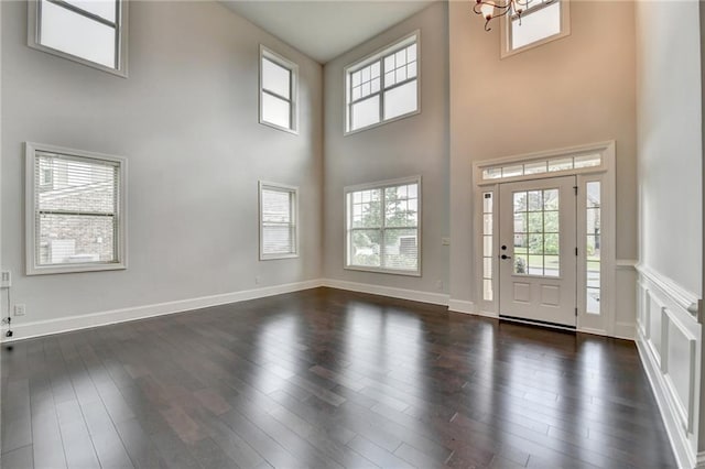 entrance foyer with a high ceiling, a notable chandelier, a wealth of natural light, and dark wood-type flooring