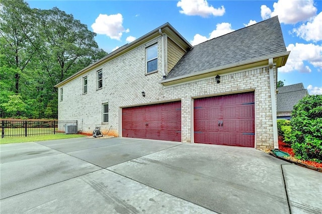 view of property exterior with fence, cooling unit, roof with shingles, brick siding, and concrete driveway