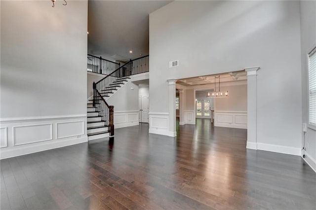 unfurnished living room featuring an inviting chandelier, a decorative wall, decorative columns, a towering ceiling, and visible vents
