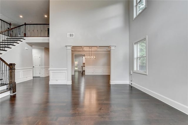 unfurnished living room featuring visible vents, stairs, a towering ceiling, and wood finished floors