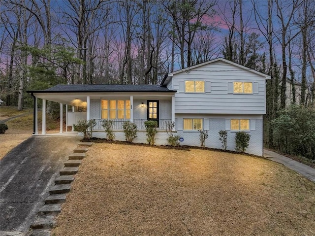 tri-level home with driveway, a lawn, an attached carport, covered porch, and brick siding