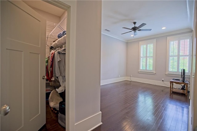interior space featuring baseboards, dark wood-style flooring, crown molding, and a walk in closet