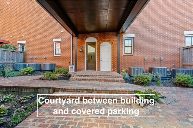 property entrance featuring central air condition unit, brick siding, and fence