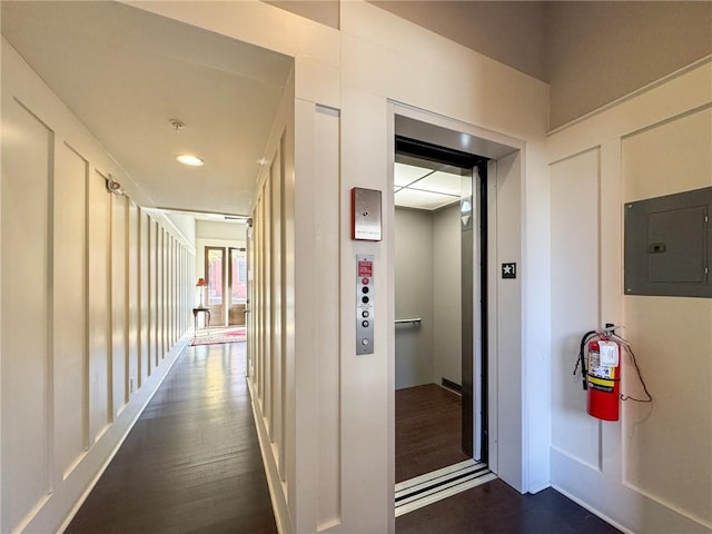 hallway featuring dark wood-type flooring, electric panel, and elevator
