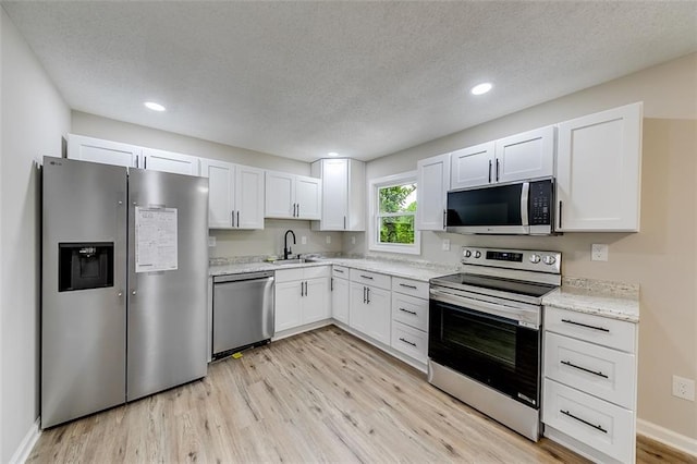 kitchen with light wood-type flooring, stainless steel appliances, white cabinets, and a sink