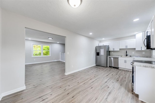 kitchen with light wood-style flooring, white cabinets, appliances with stainless steel finishes, and baseboards